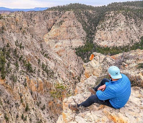 A hiker dressed in blue sits on a rocky cliff looking at limestone canyons in Escalante, Utah