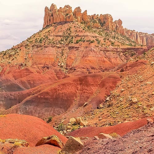 A large multi-colored orange, purple, red, and yellow desert butte is located at Capitol Reef National Park in Utah.