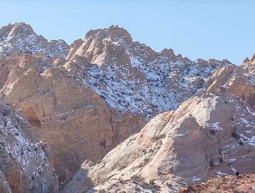 A hiker stands to the right looking at a snow-covered mountain with cream-colored buttes.