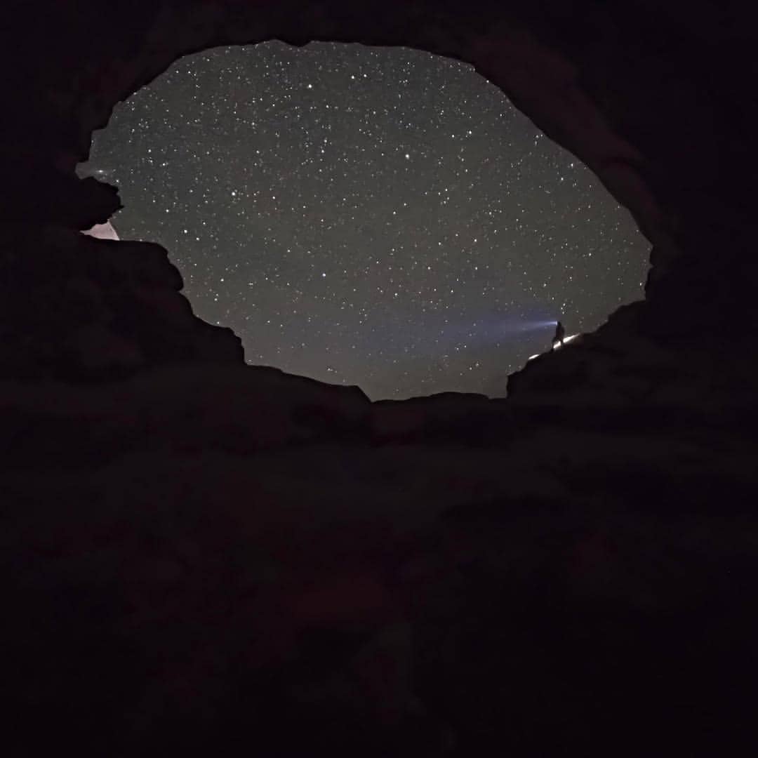 A hiker with a headlamp stands inside a window rock formation that reveals the starry night sky at Arches National Park in Moab, Utah
